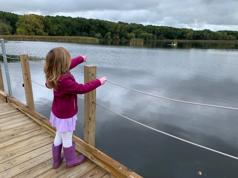 A young girl points across a large pond toward a white bird at Wood Lake Nature Center in Richfield, Minnesota.