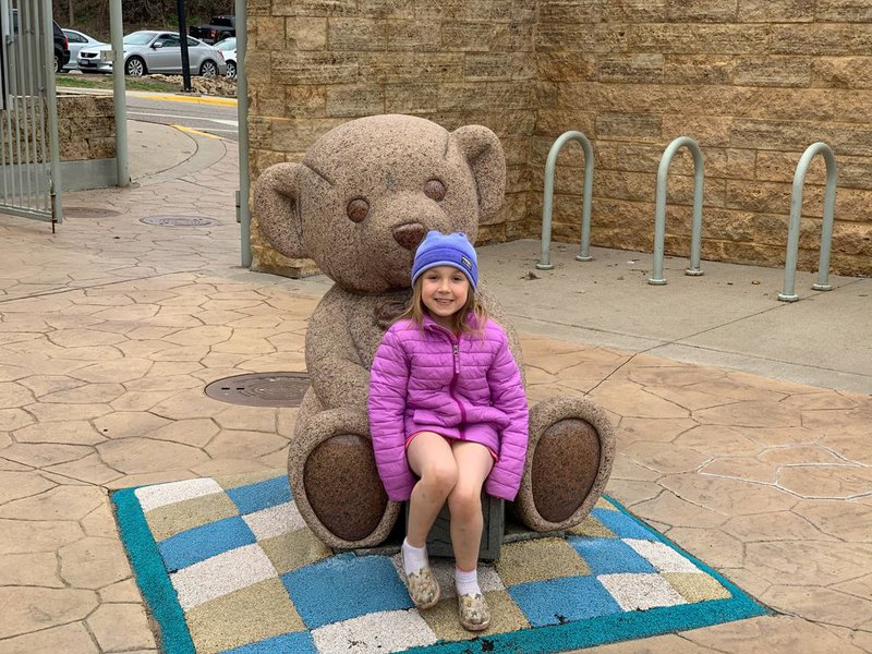 A young girl sits on the lap of a stone teddy bear at a playground in Stillwater.