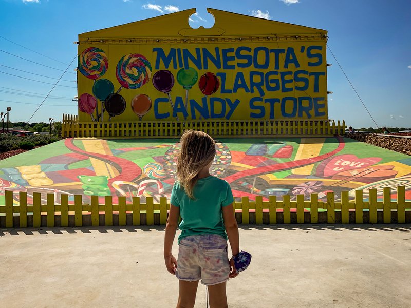 A young girl stands looking at a sign that reads "Minnesota&#x27;s Larges Candy Store".