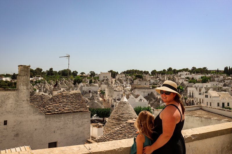 A mom and her daughter stand on a city terrace looking out onto the trulli of Alberobello.